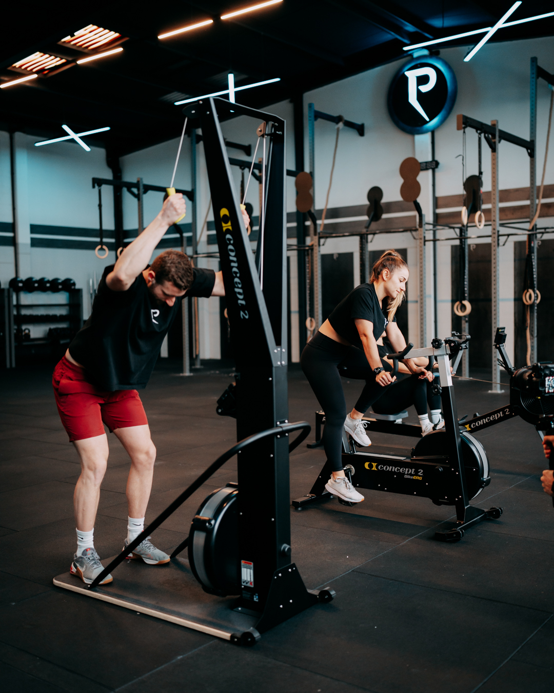 Coach beim Training mit Kunde an Concept2-Geräten im Peak Vitality Gym